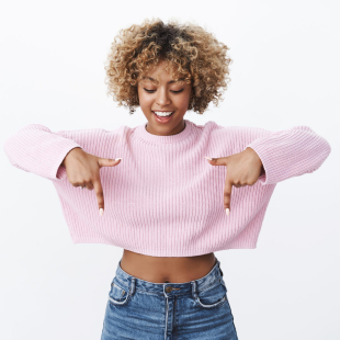 Curious and stylish fashionable african-american girl with blond curly haircut looking interested with broad smile as pointing down intrigued with cool amazing promotion over white background. Advertisement concept